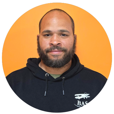 Person with a beard wearing a black hoodie against an orange background.