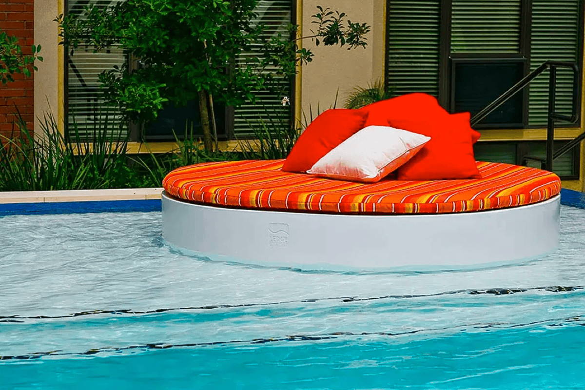 Round in-pool daybed with vibrant orange cushions and outdoor throw pillows. 