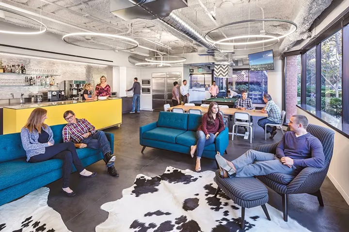 People socializing in a modern office lounge with blue sofas and a cowhide rug.