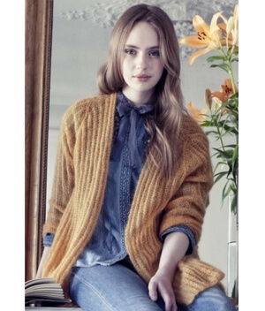 Young woman in a cozy sweater, sitting near a mirror with flowers.