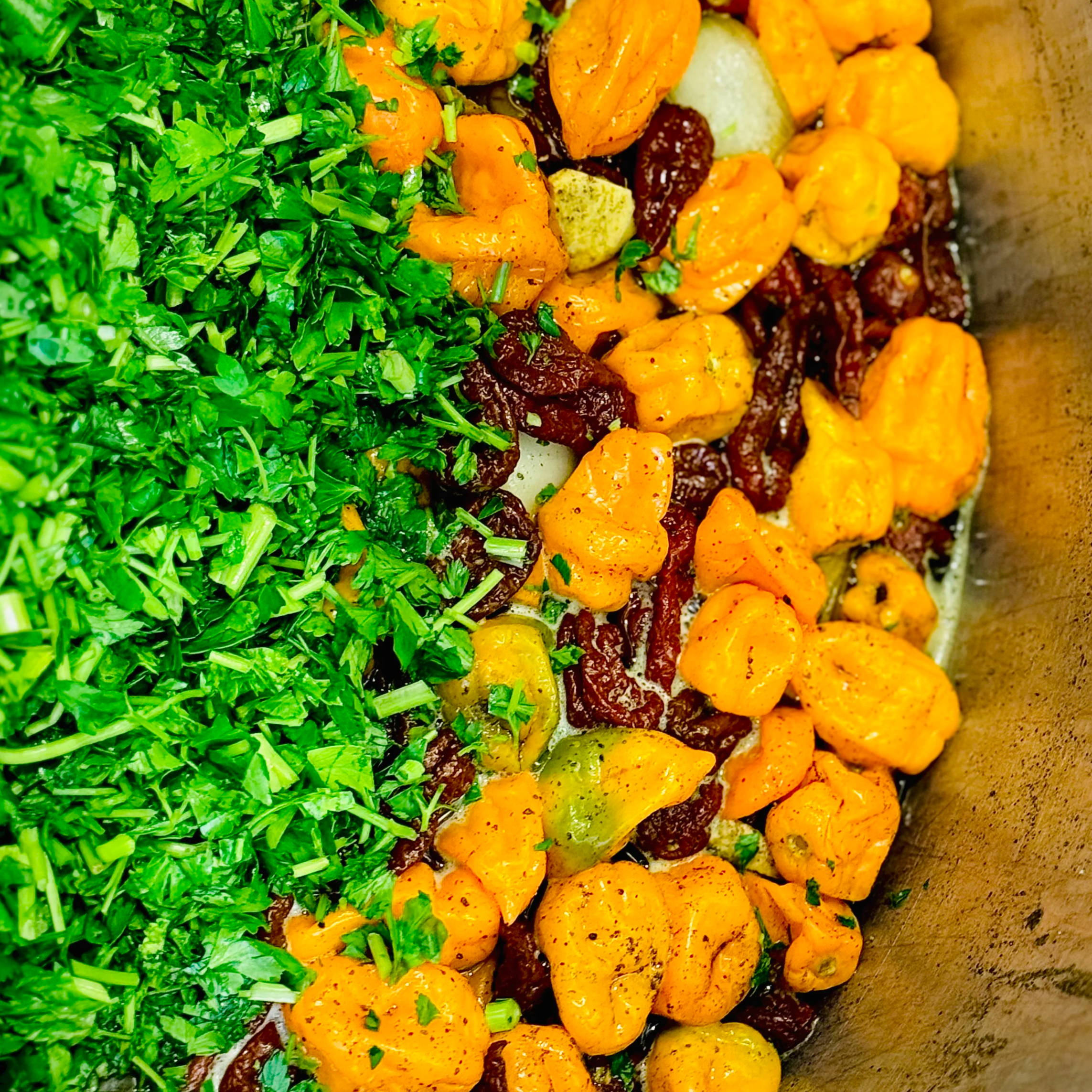 Chopped herbs, orange vegetables, and dried fruits in a cooking pot.