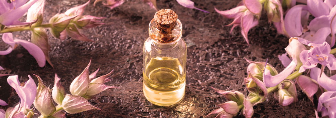 Glass bottle of oil surrounded by purple flowers.