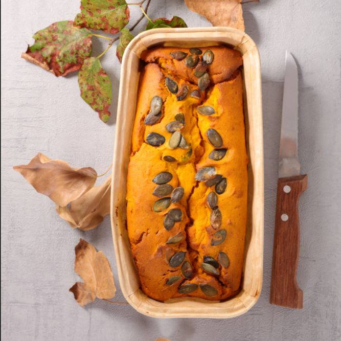 bright orange pumpkin loaf with sprinkled seeds on top on a table with leaves and a knife