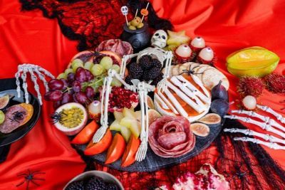 A Halloween-themed platter with fruits, snacks, and skeleton decorations on a red background.
