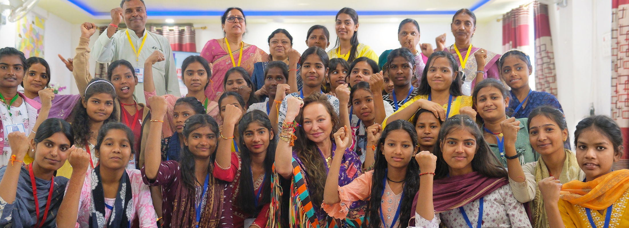 A large group from The Butterfly Effect in a hall in Bihar, many raising a strong arm to the camera, Camilla Franks among them.