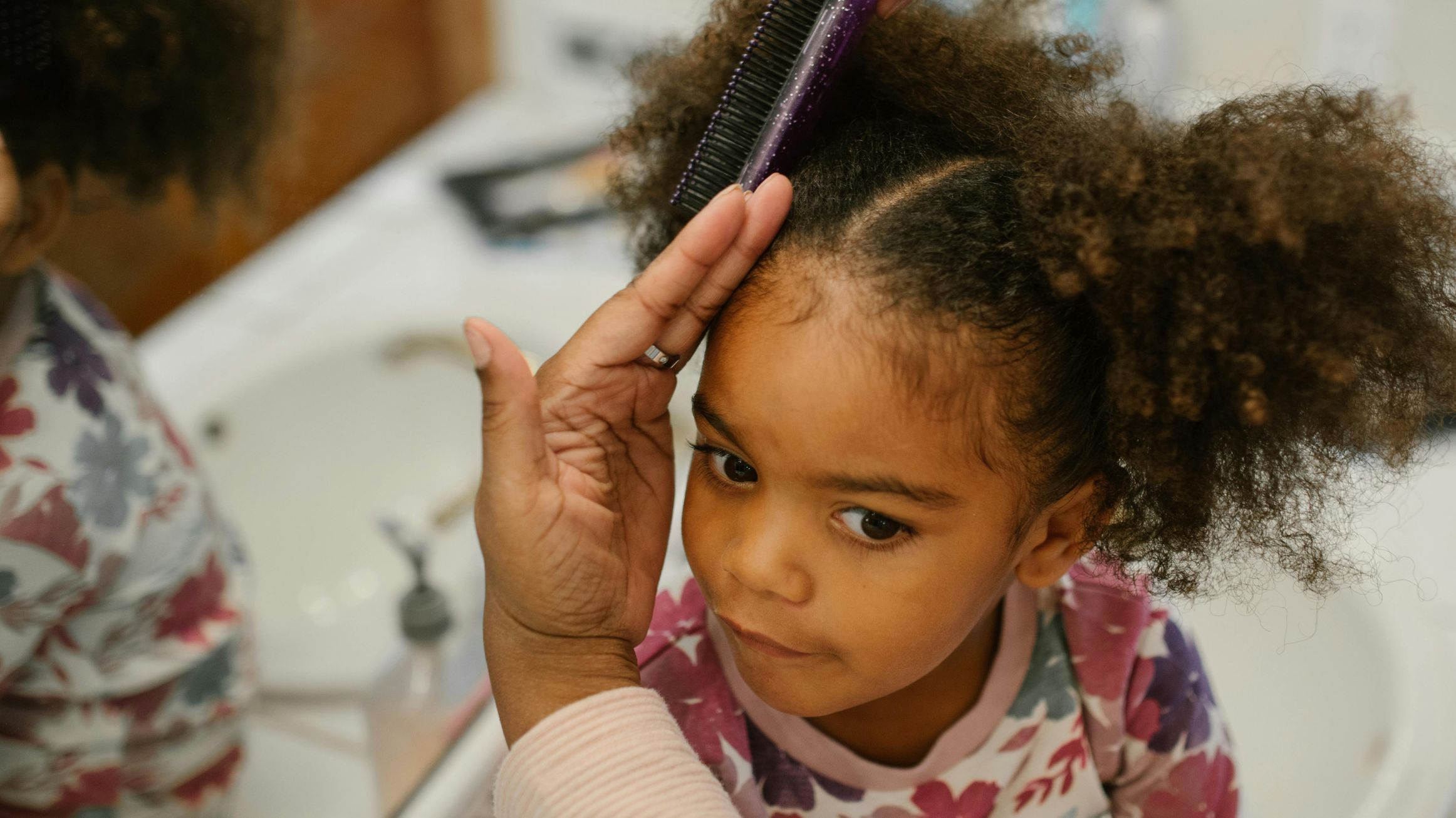 A child with curly hair getting styled in front of a mirror.