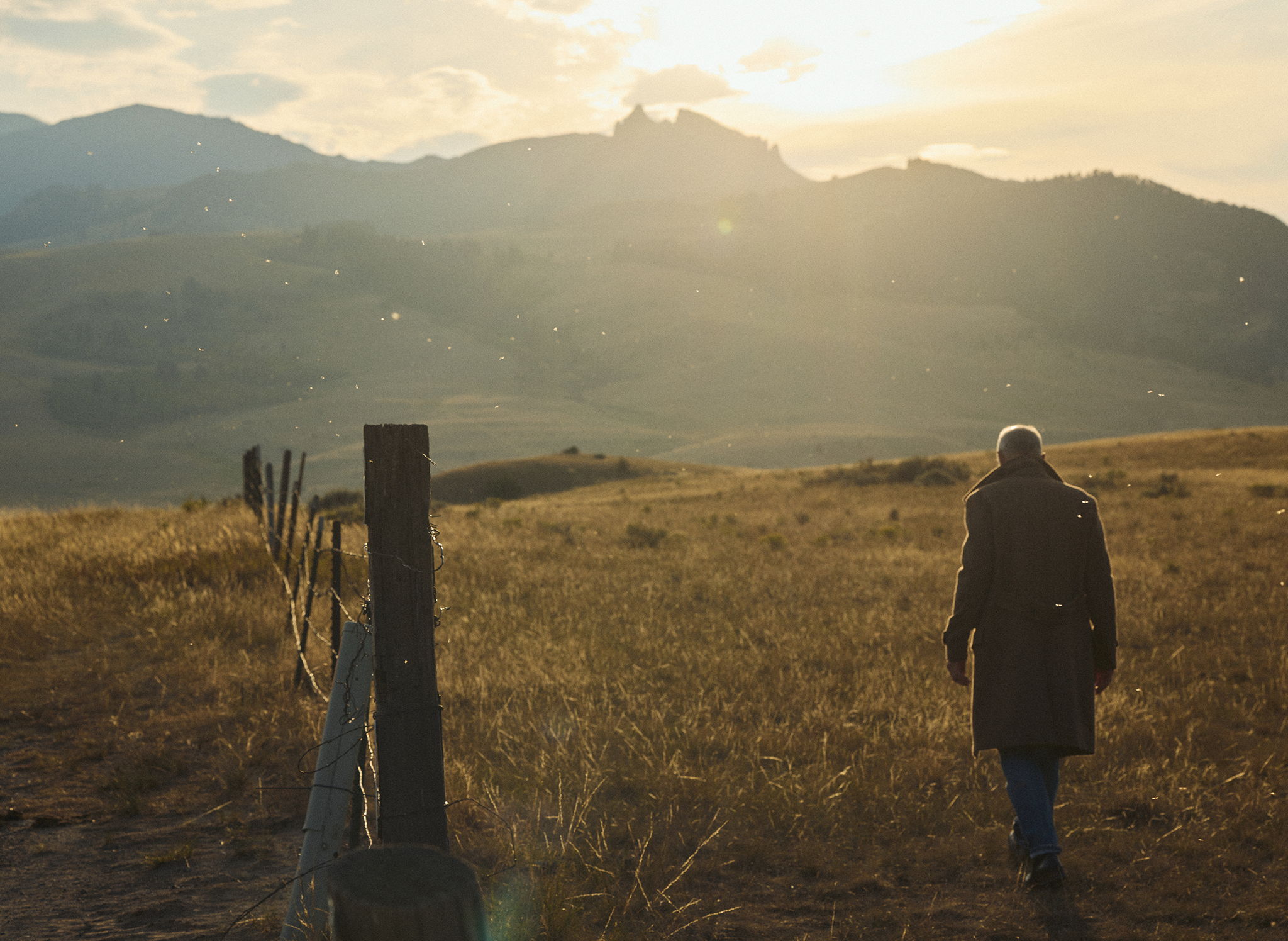 Michael Kelly wearing the Barrow Wool Herringbone Double Breasted Topcoat in a Montana Field with a barbed wire fence and mountains in the background