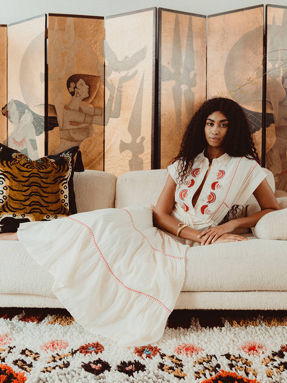 A girl laying on the couch wearing a white embroidered dress