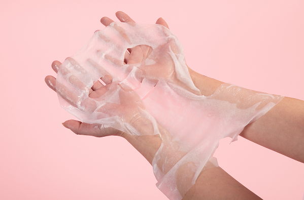Hands wearing transparent gloves against a pink background.