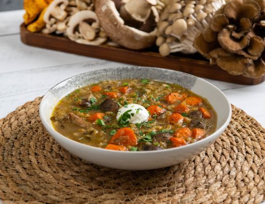 Bowl of soup with vegetables and herbs on a woven placemat.