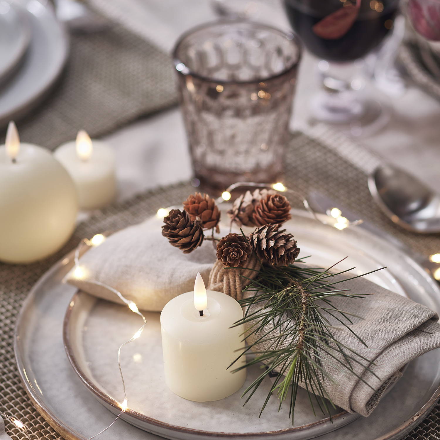 A Christmas place setting with candles, micro lights and festive pinecones 