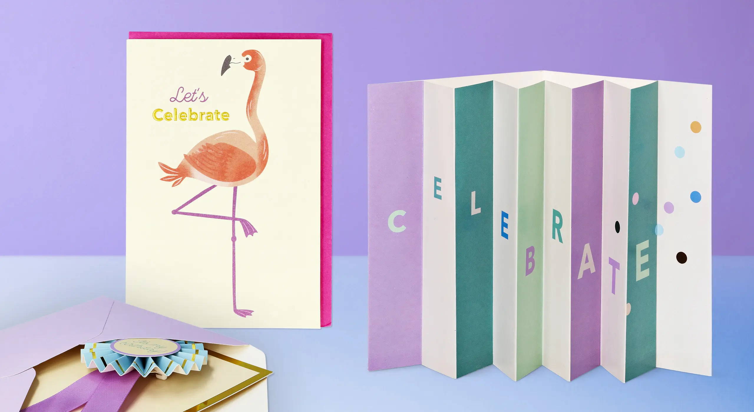 Et 'Let's Celebrate'-flamingokort ved siden af harmonika-foldede festkort i pastelfarver