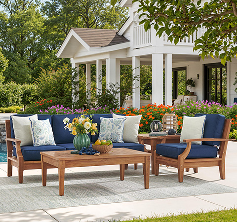 Outdoor seating area with cushions, coffee table, and colorful flowers.