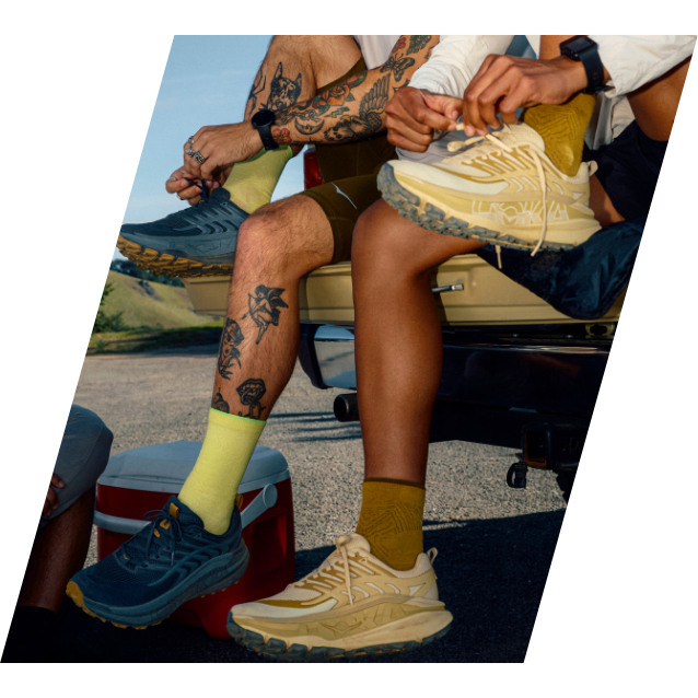 Two people wearing colorful shoes and socks, sitting by a vehicle.