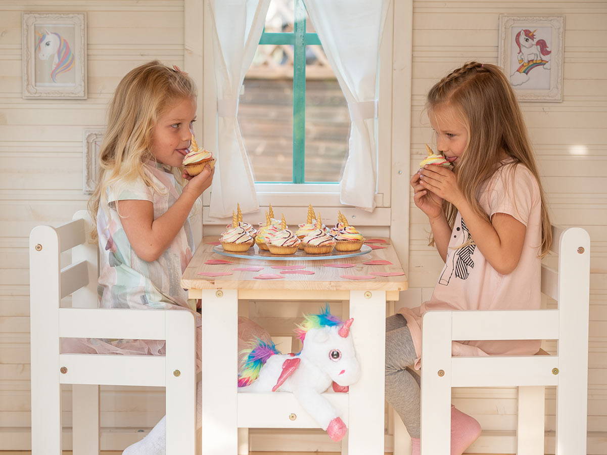 Two kids eating inside of kids wooden playhouse with kids furniture set by WholeWoodPlayhouses