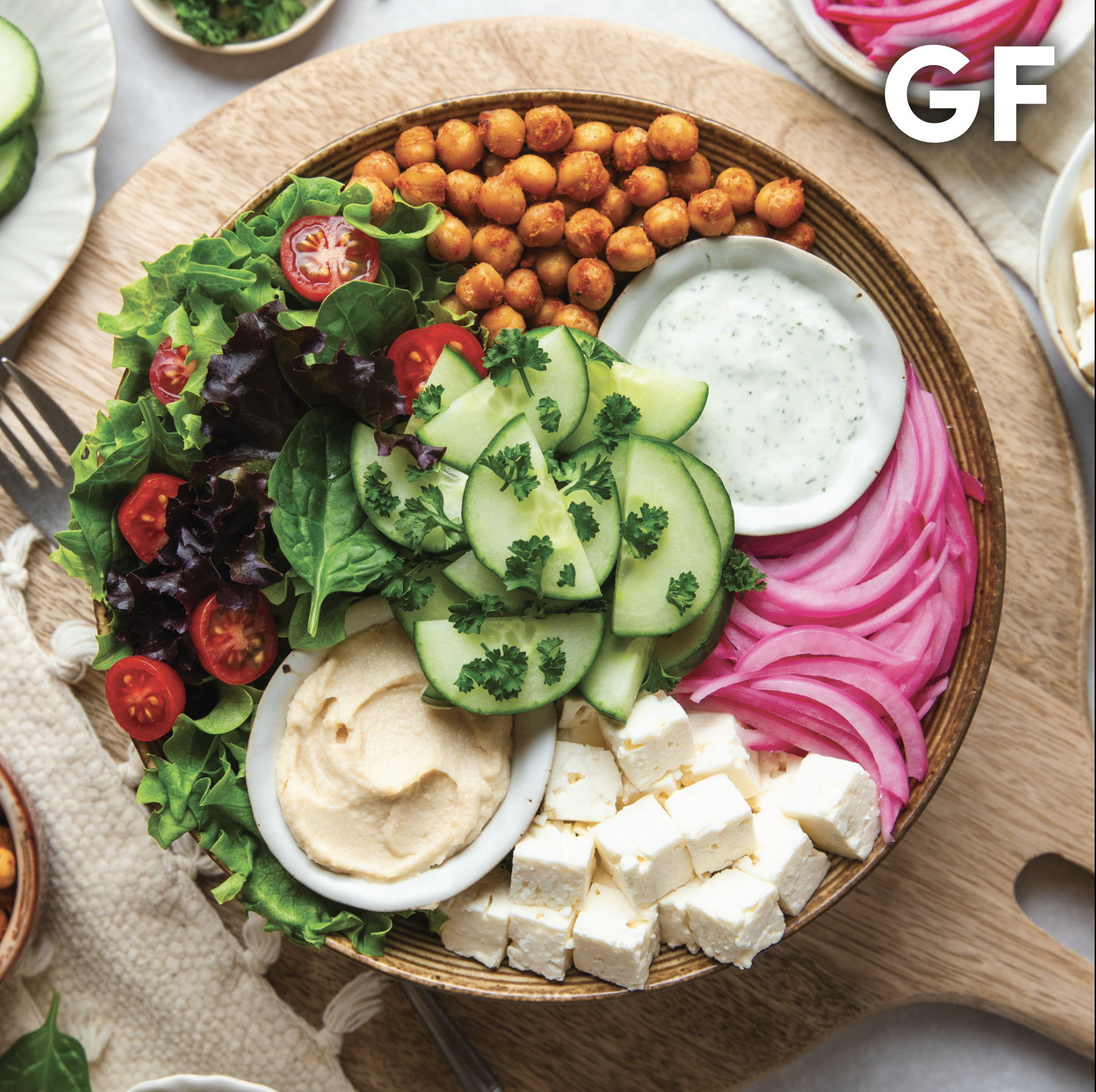 A colorful salad bowl with vegetables, hummus, and cheese. Gluten-free label visible.