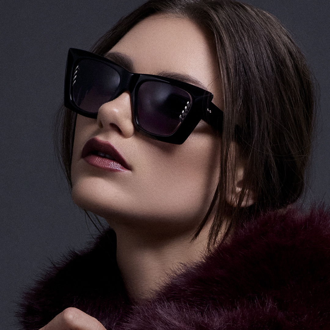 Woman wearing sunglasses and a fur coat against a dark background.