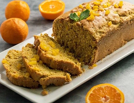 Sliced orange loaf cake with whole oranges on a white platter.