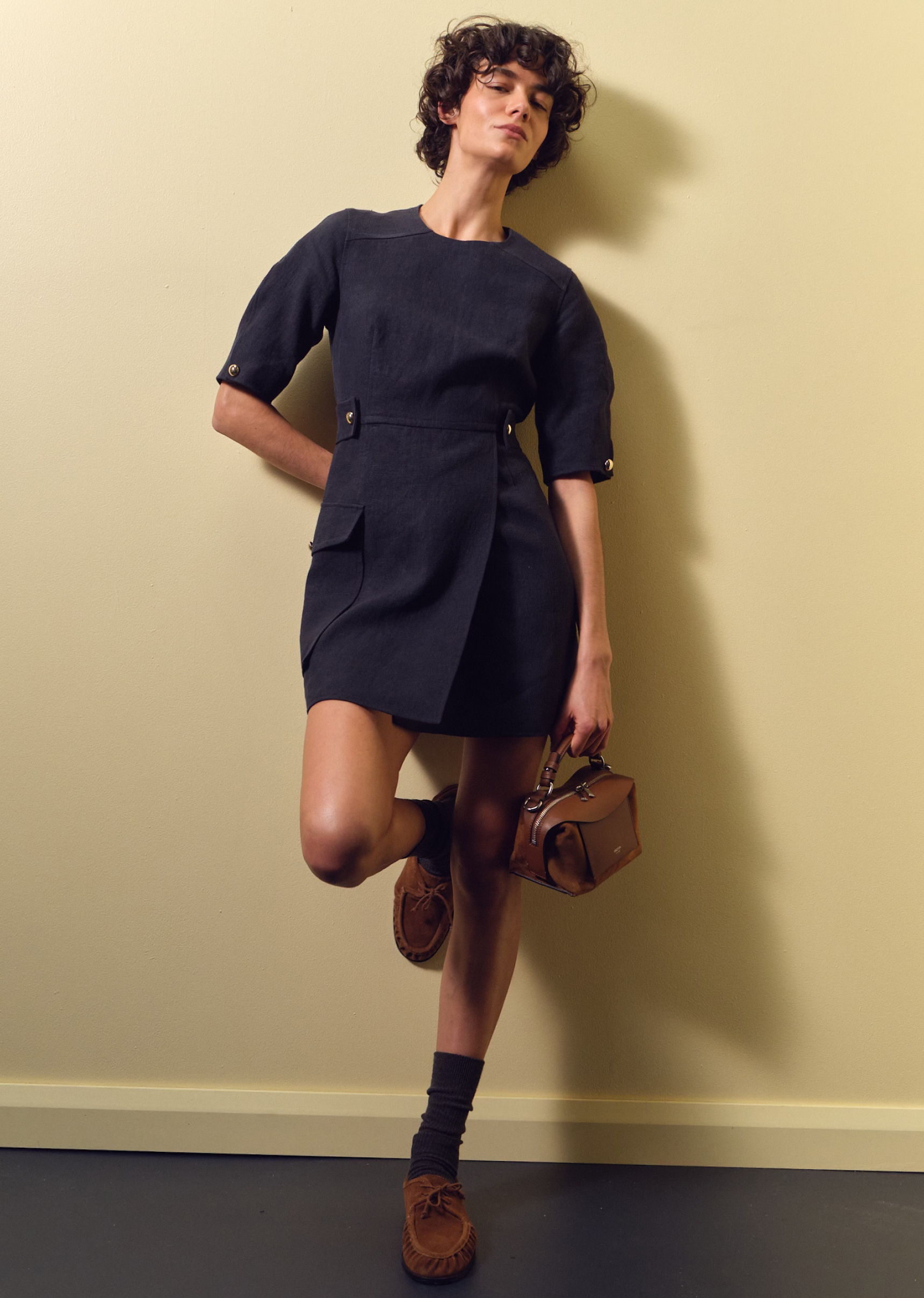 A model poses in a dark dress against a neutral background.