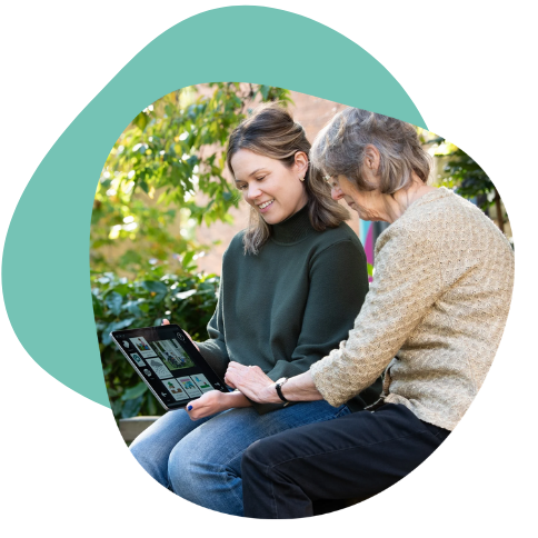 Two women sharing a moment while looking at a tablet outdoors.