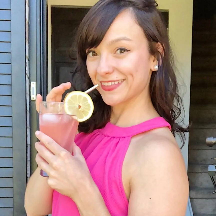 Women with bright pink top sips True Lemon drink from a glass with a Lemon slice 