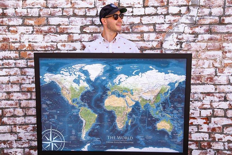 Person holding a world push pin travel map with a brick background