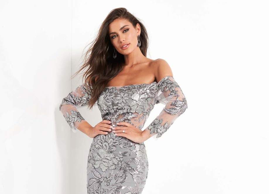 Woman in silver floral off-shoulder dress poses against a white background.