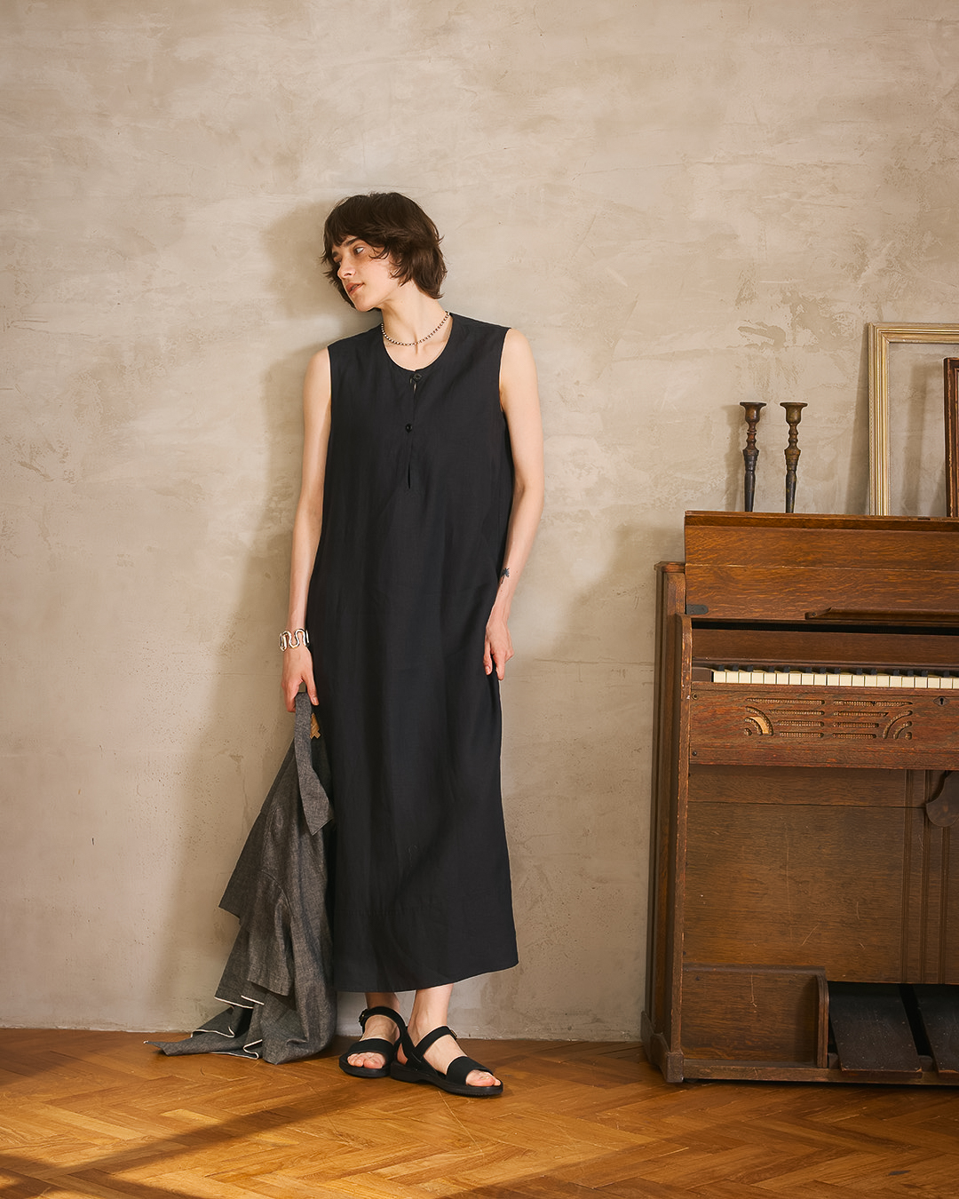Woman in stylish outfit standing next to a vintage piano in a cozy setting.