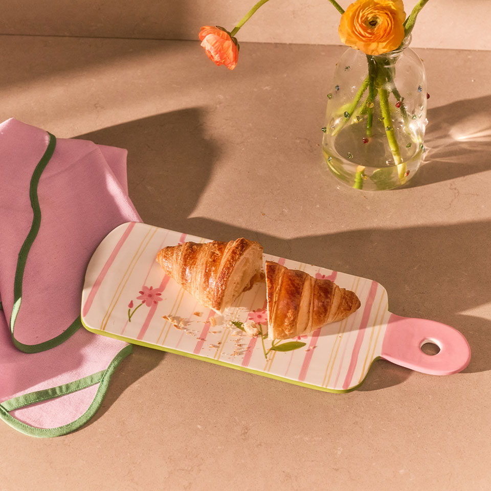 A croissant on a decorative cutting board with a vase of flowers.