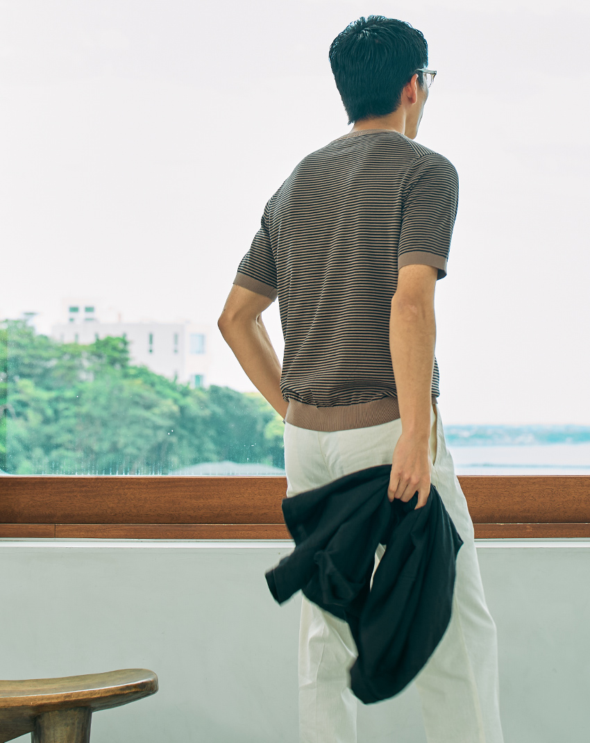 A man walking indoors near a large window with greenery outside.