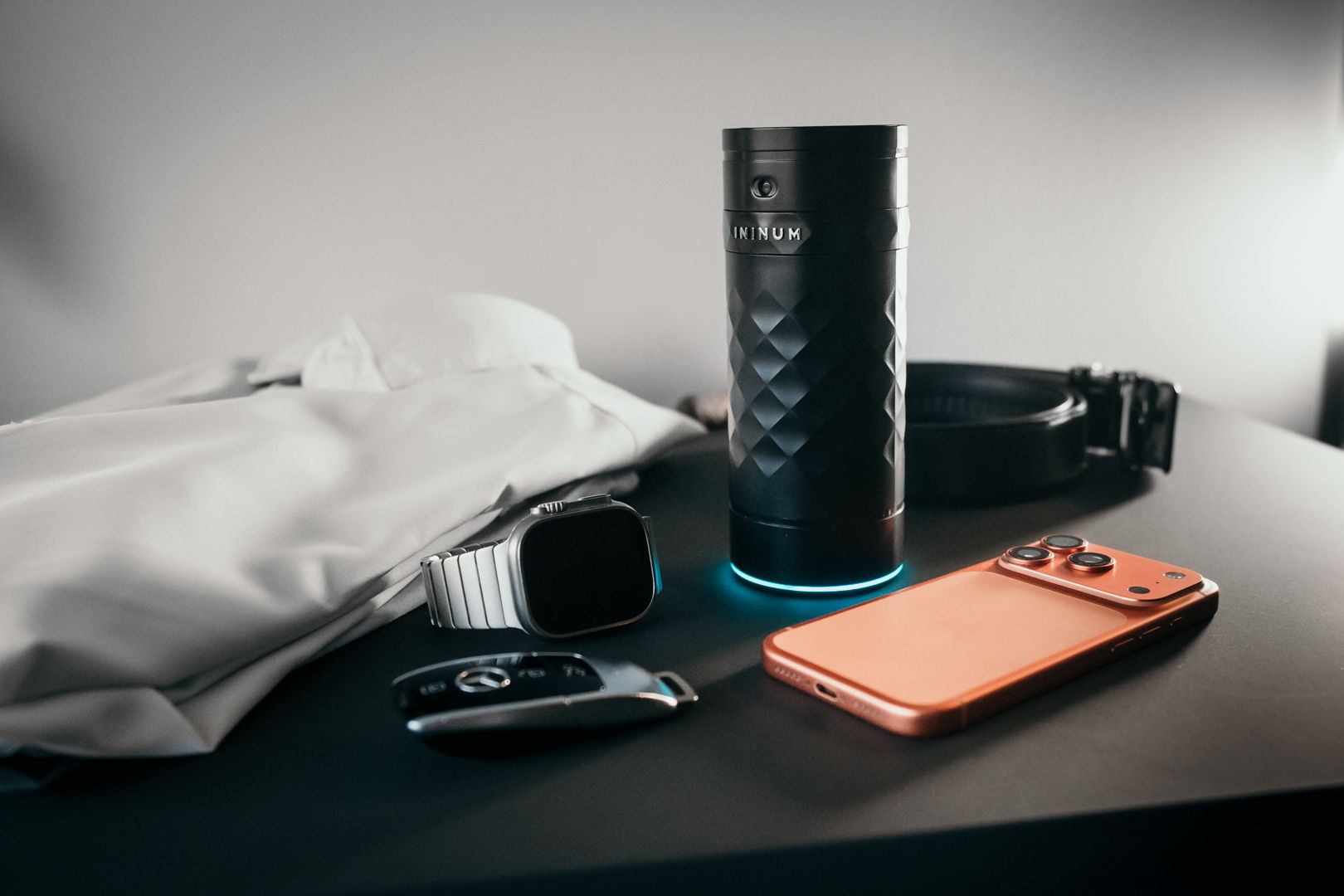 A smartphone, smartwatch, speaker, keys, belt, and a bag on a table.