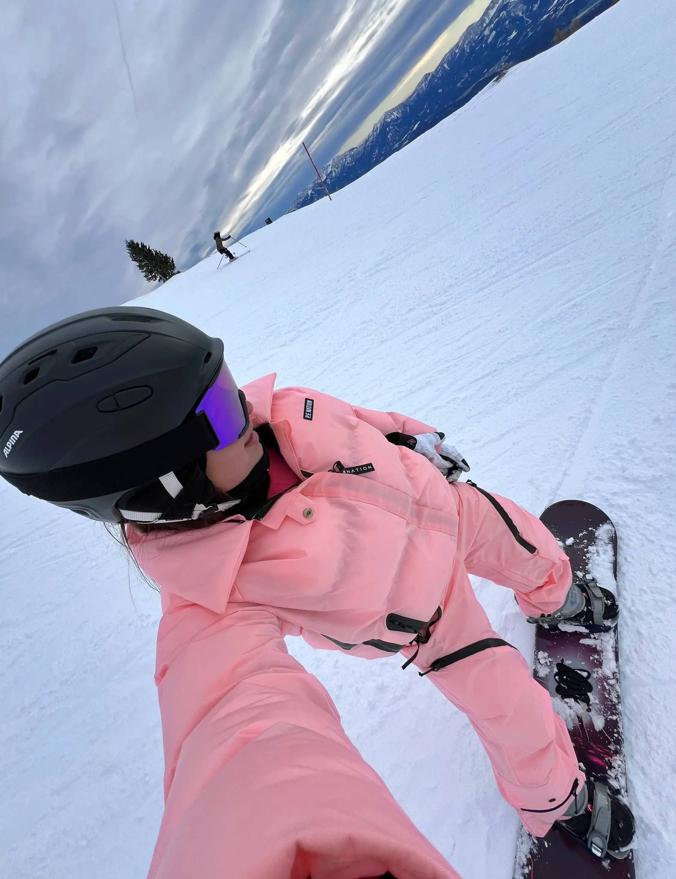 Girl wearing a pink ski suit, she is snowboarding
