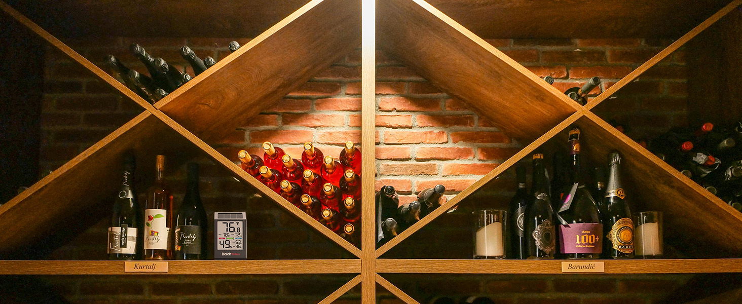 Wine bottles arranged on wooden shelves with brick background.