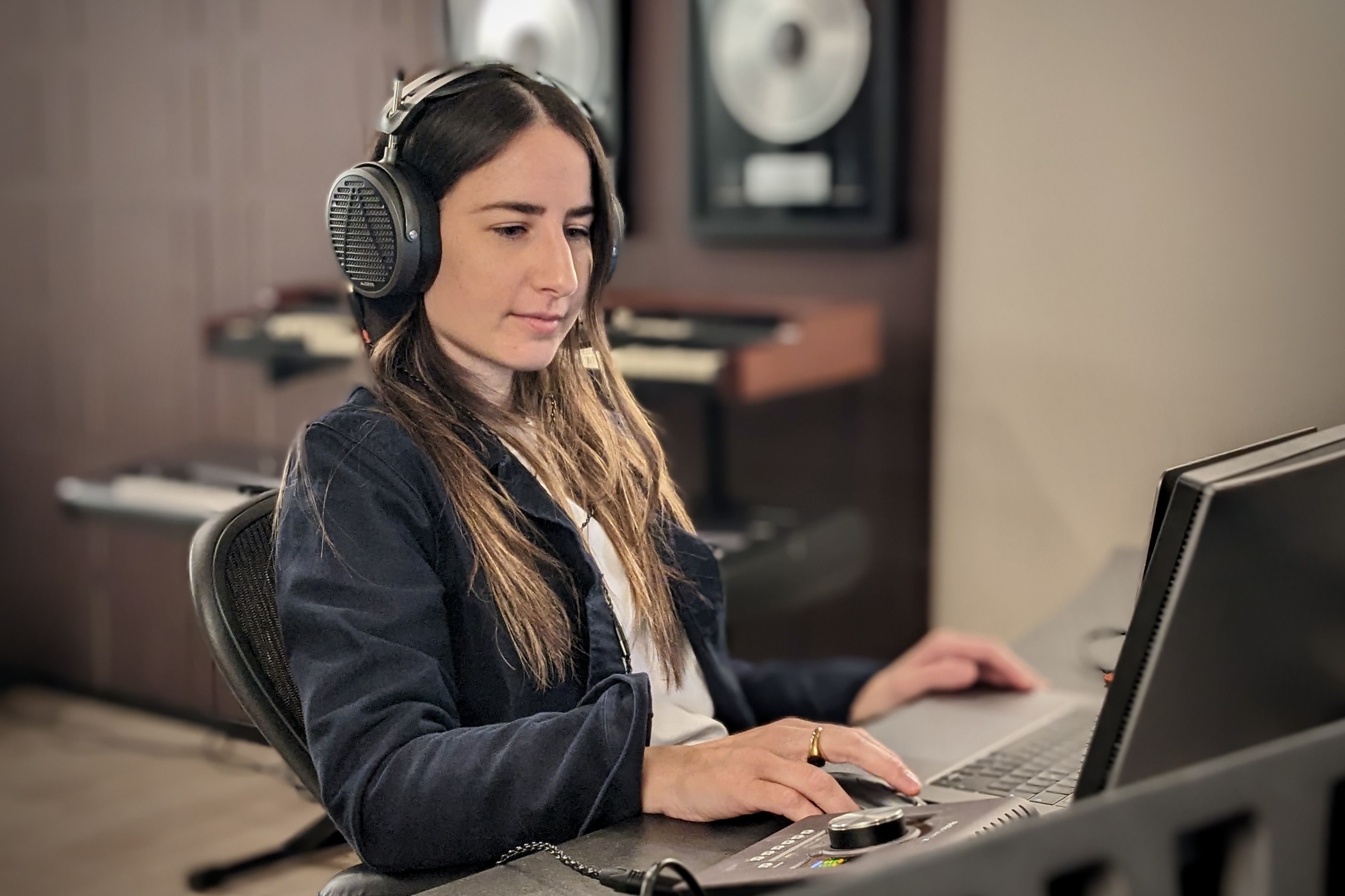 Amanda Merdzan wearing Audeze MM-500 headphones working on a computer in a music studio.