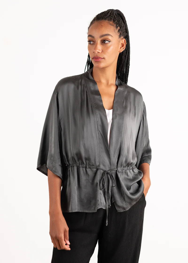 A model wearing a dark grey satin jacket with a draw string waist and kimono style sleeves
