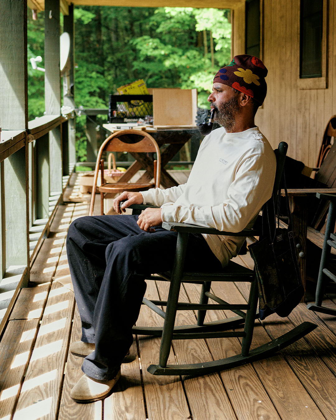 Person sitting in a rocking chair on a porch surrounded by greenery.