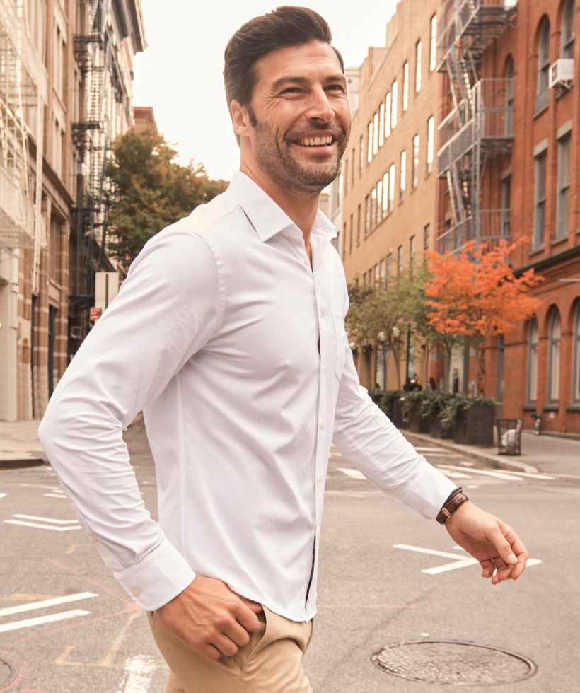 A man in a white shirt walking down a city street, smiling.