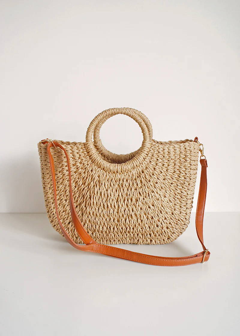 A wicker basket with circular handles and brown detachable shoulder strap