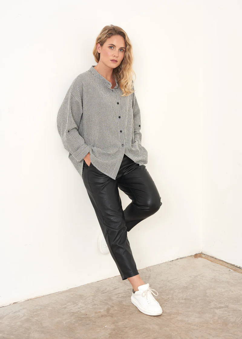 A model wearing a grey and white check oversized shirt with black faux leather trousers and white trainers