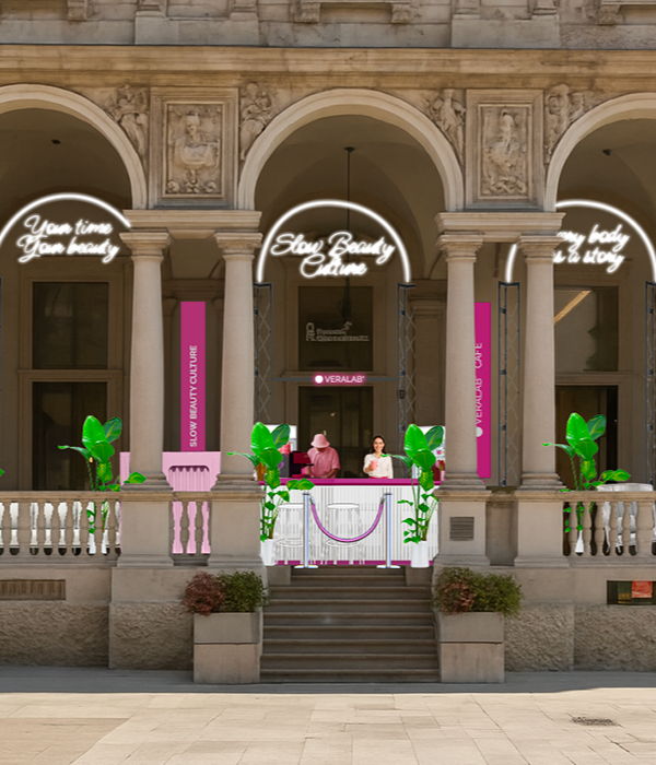 Two people in front of a building with decorative plants and signage.