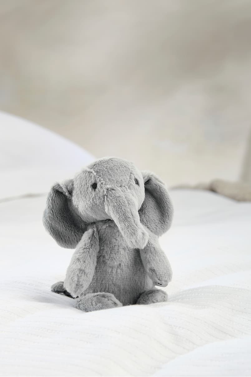 A cute gray stuffed elephant sitting on a light-colored surface.