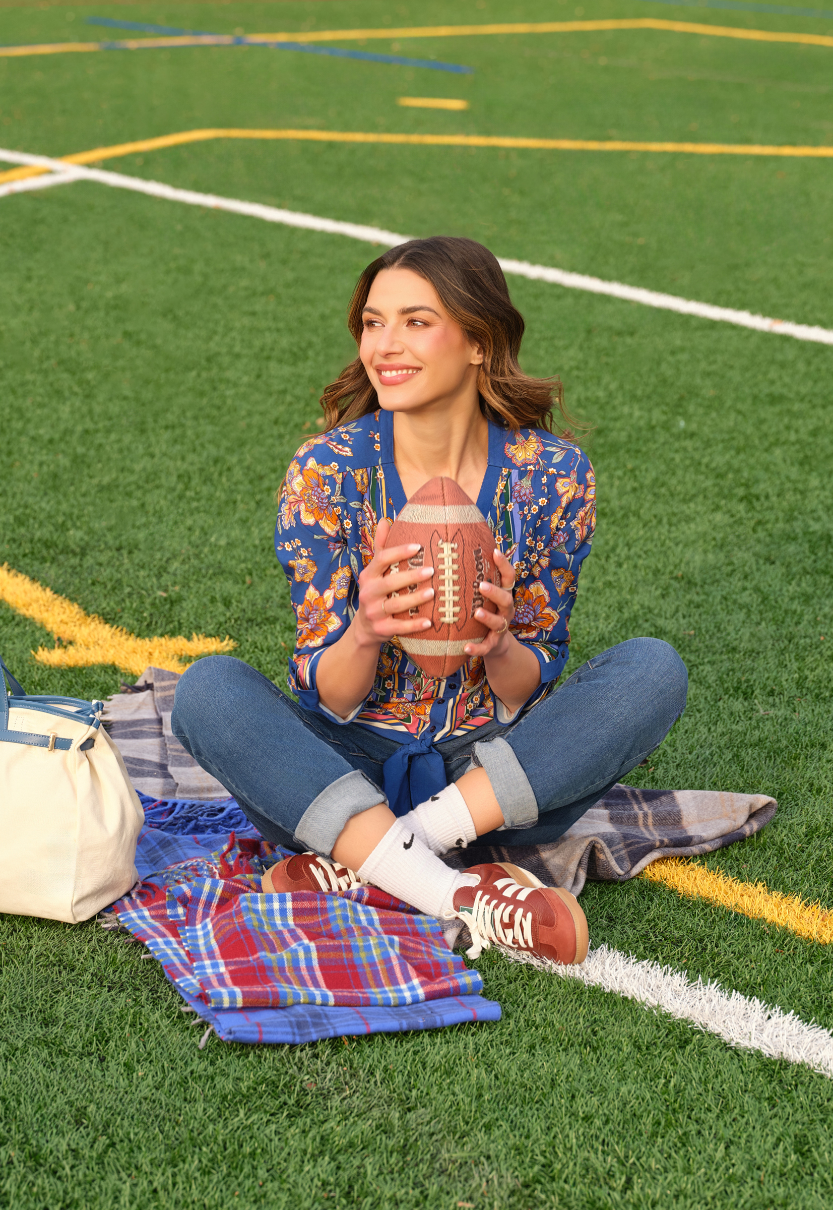 Young woman sitting on grass, holding a football, smiling.