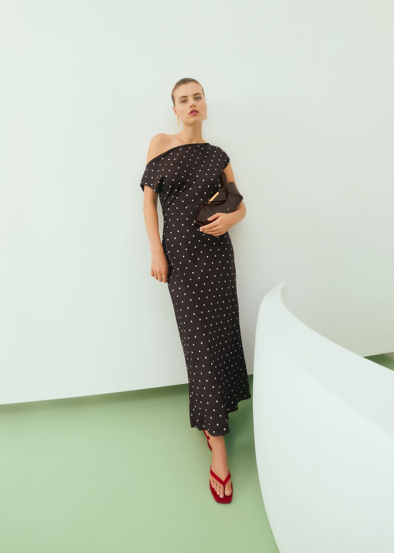 Woman in a black off-shoulder dress standing against a white wall.