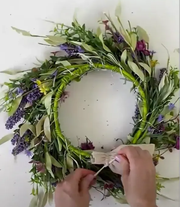 Person tying the drawstring of her linen bag to the frame of the back of the wreath.