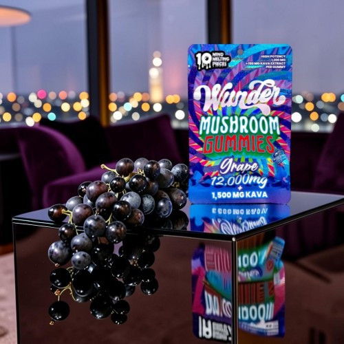 A box of mushroom gummies beside a cluster of grapes on a reflective surface.