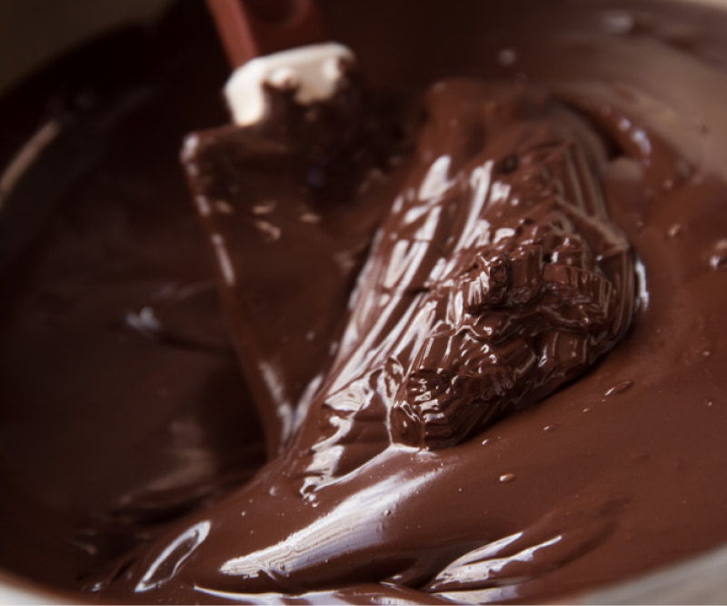 A bowl of melted chocolate with a spatula mixing it.