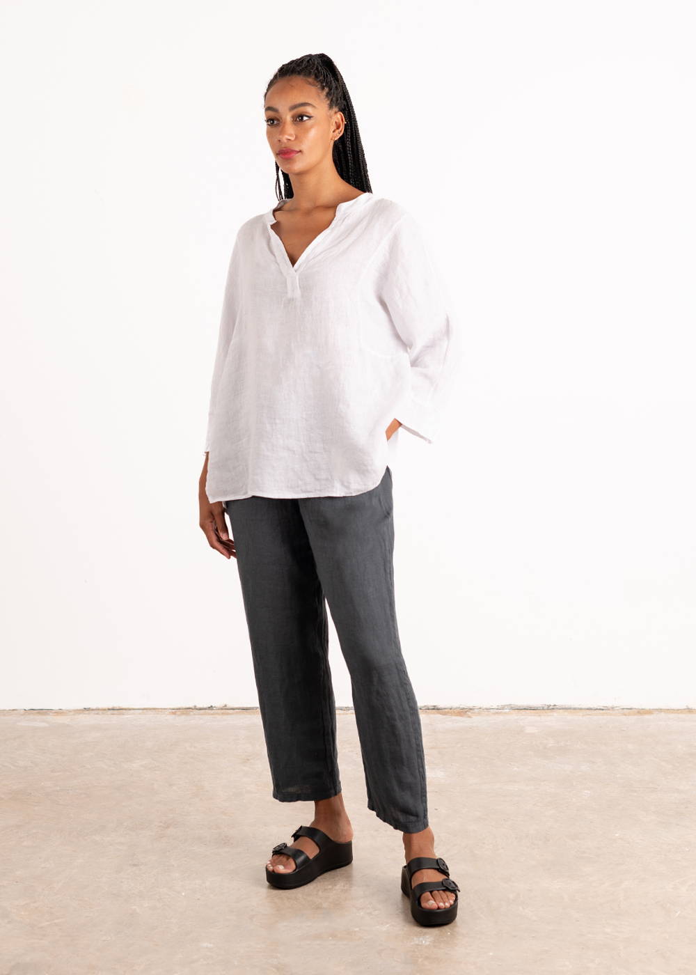 A model wearing a relaxed fitting linen blouse with  long sleeves with some dark grey linen trousers and black chunky slides 