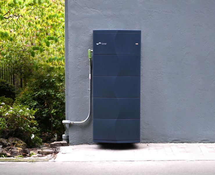Lunar Energy battery unit against a gray wall with greenery.