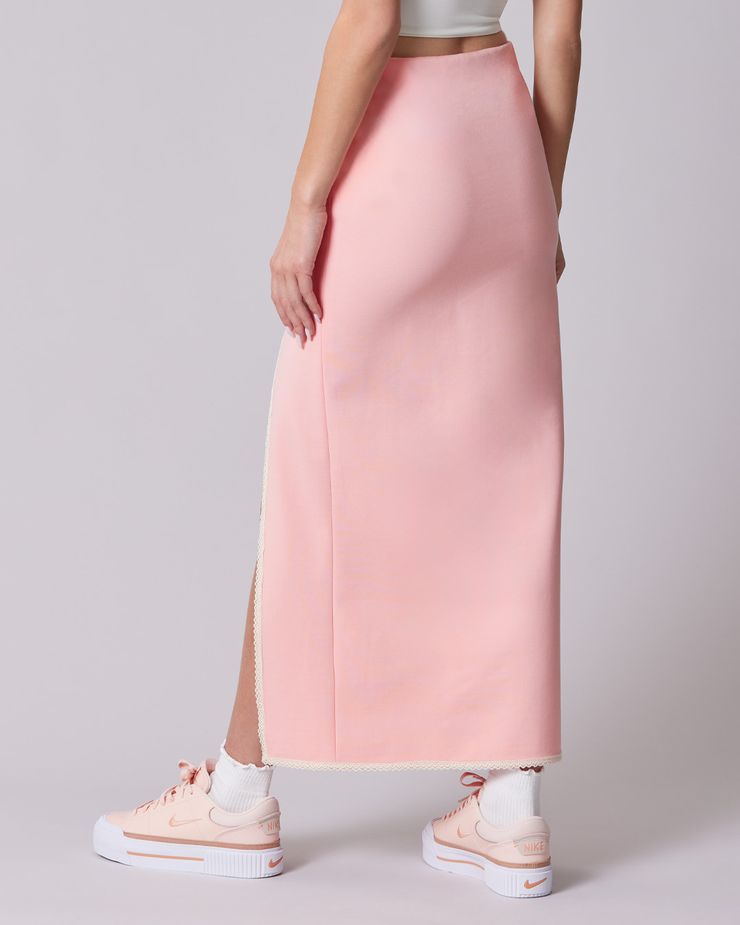 Woman in a white crop top and pink skirt, holding a pink bag.