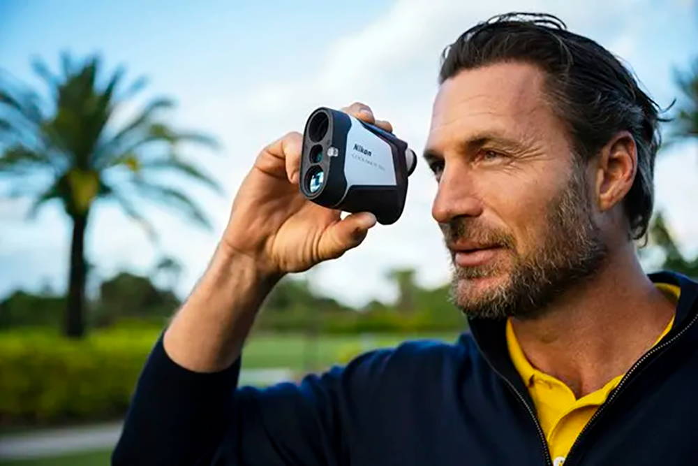 A man holding a Nikon golf rangefinder on a golf course with palm trees